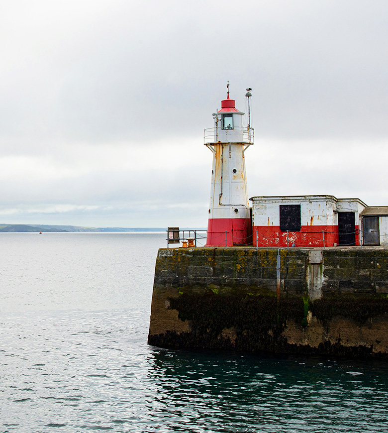 A picturesque view of Newlyn Lighthouse perched on a pier, surrounded by the tranquil waters of Mount's Bay.