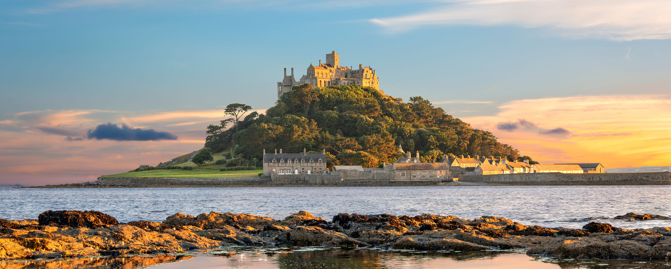 Sunset over St Michael's Mount, Mount's Bay, highlighting its silhouette against a vibrant sky, reflecting on the water below.