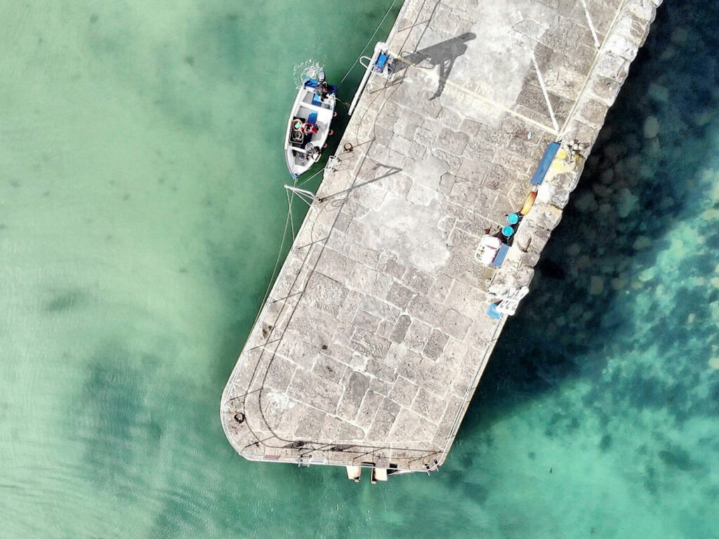 Aerial view of Mousehole Harbour, near Mount's Bay, showcasing boats docked in the ocean with vibrant blue waters surrounding them.