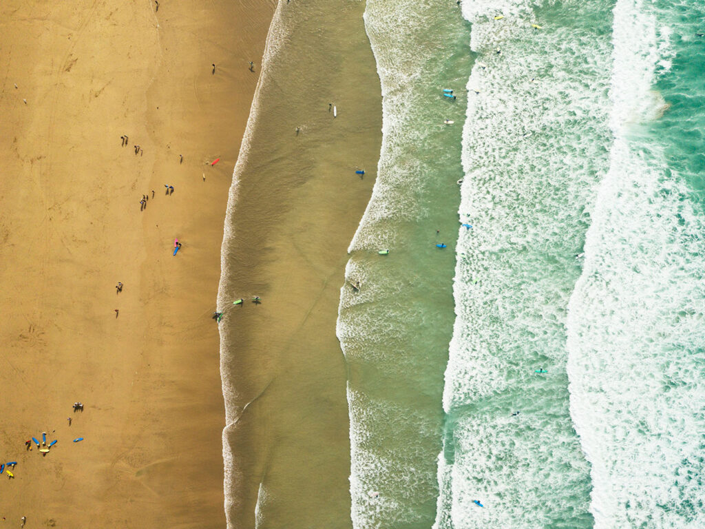 Aerial view of Fistral Beach in Newquay, showcasing people enjoying the surf and sun at a busy surf school, a great thing to see and do in Newquay.