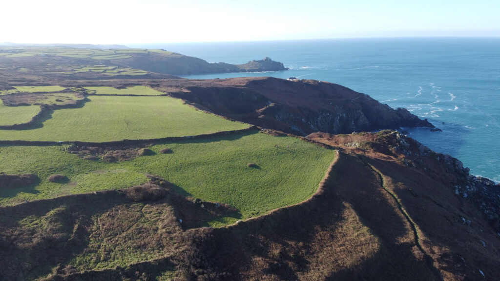 Aerial view of Zennor, showcasing a grassy hill overlooking the ocean, inspiring D.H. Lawrence's literary works.