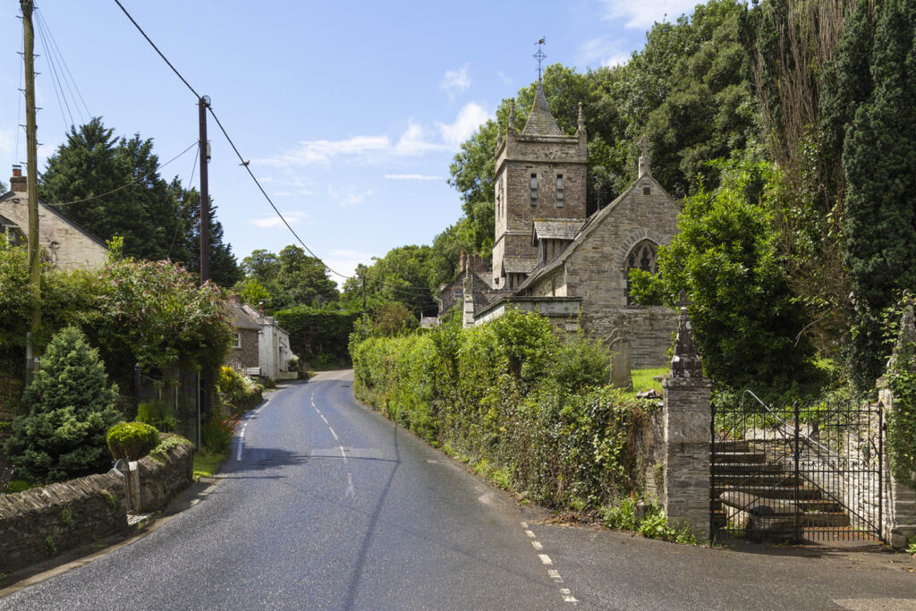 A small road lined with greenery, featuring a quaint church beside it in Little Petherick near Padstow, a great secret spot for locals.