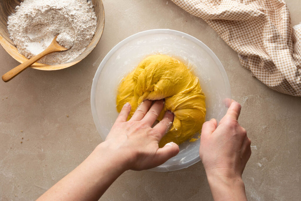 A person holds a bowl of bright yellow dough, preparing to make saffron buns, a great Cornish recipe, for Mother's Day.