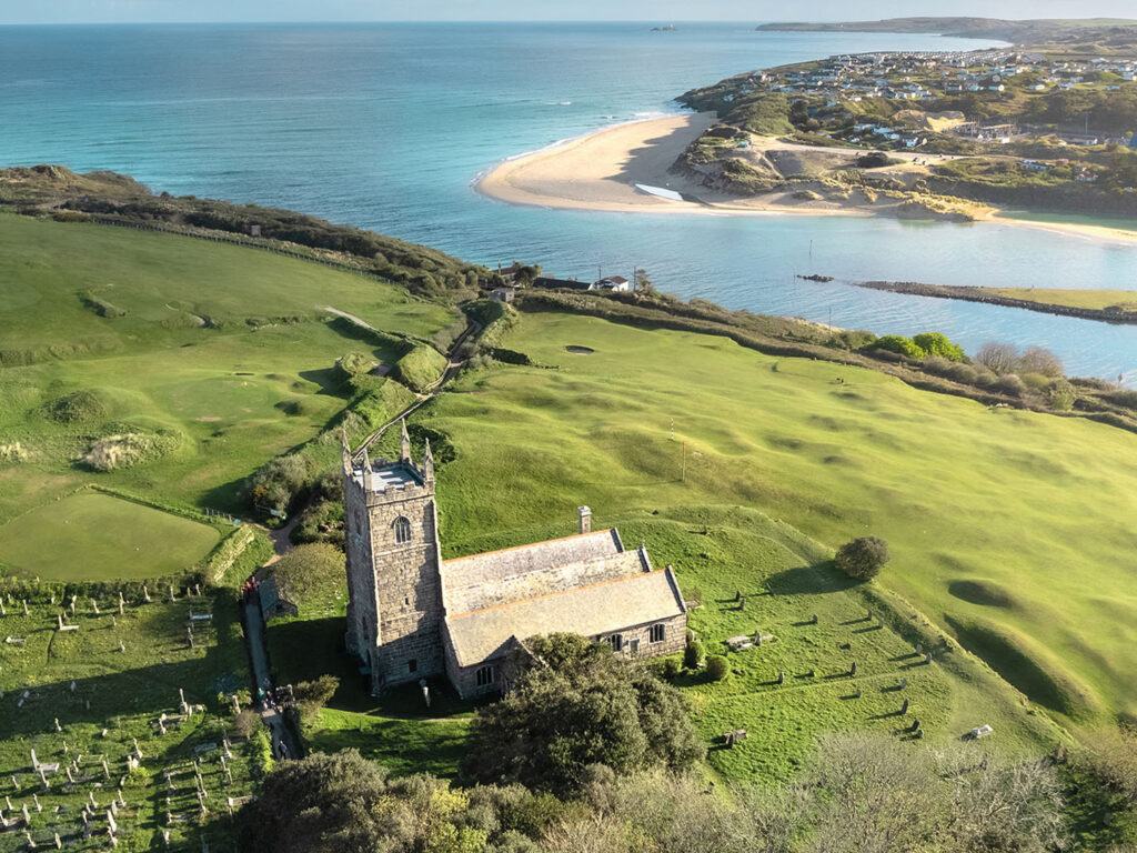 Aerial view of St. Uny Church in Lelant with surrounding graveyard and adjacent beach, just one of many locations that Cornish Escapes can help with holiday cottage ownership.