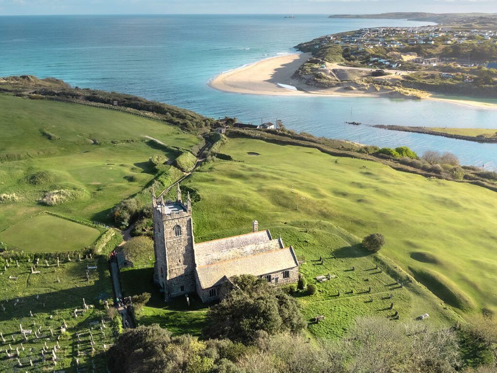 Aerial view of St Uny Church and the beach in Lelant, showcasing the scenic coastline and nearby West Cornwall Golf Club, a great thing to do in Carbis Bay.