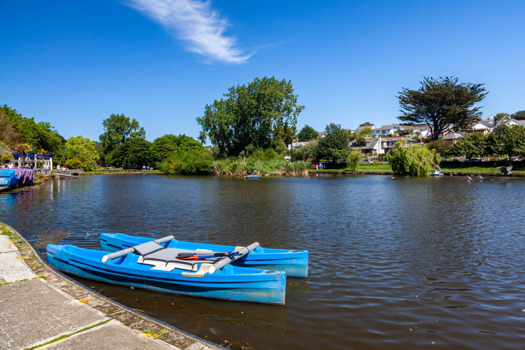 Two boats are docked peacefully on Newquay's scenic boating lake, surrounded by tranquil waters and greenery, a great thing to do in Newquay off the beaten track.