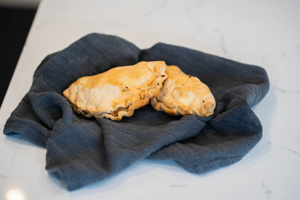 Two golden Cornish pasties resting on a blue cloth atop a counter, a perfect recipe for a Mother's Day treat.