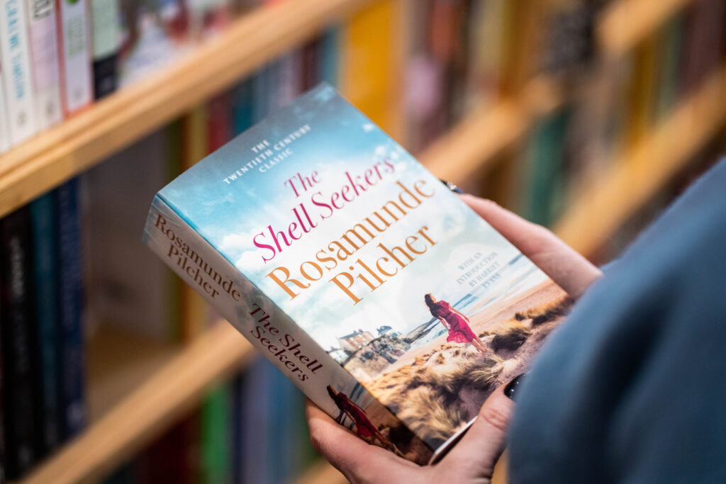 Woman holding 'The Shell Seekers' by Rosamunde Pilcher, an author inspired by her Cornish upbringing.