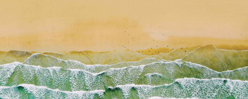 Aerial view of Carbis Bay Beach, featuring waves and birds soaring over the vibrant ocean, a great location for Cornwall holiday cottages.