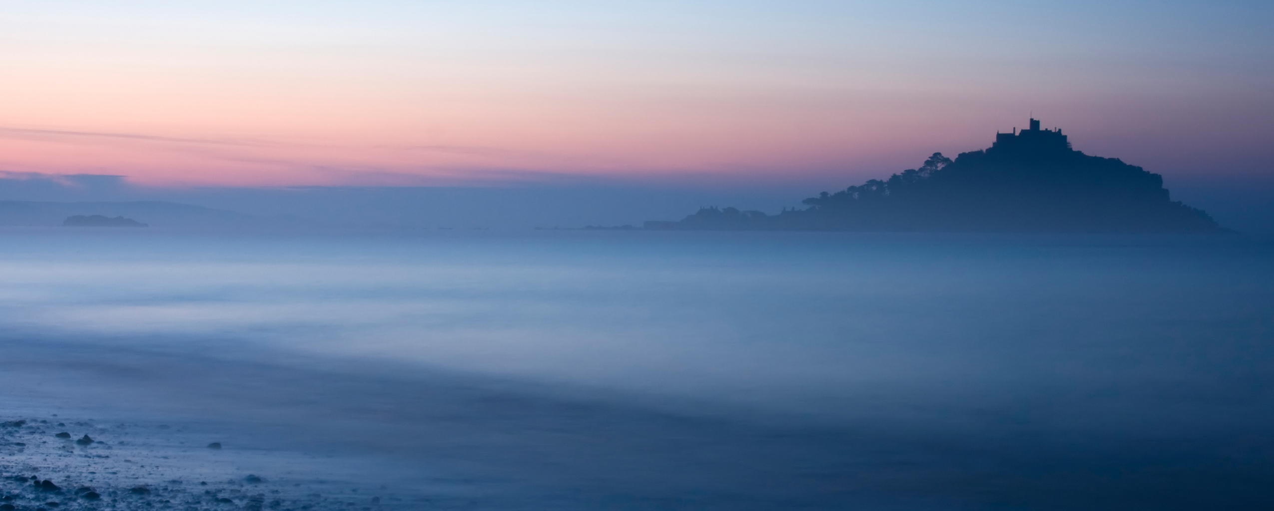 Dusk over St Michael's Mount, shrouded in mist and fog, creating a mystical atmosphere, visit after reading our Privacy Policy and booking with Cornish Escapes.