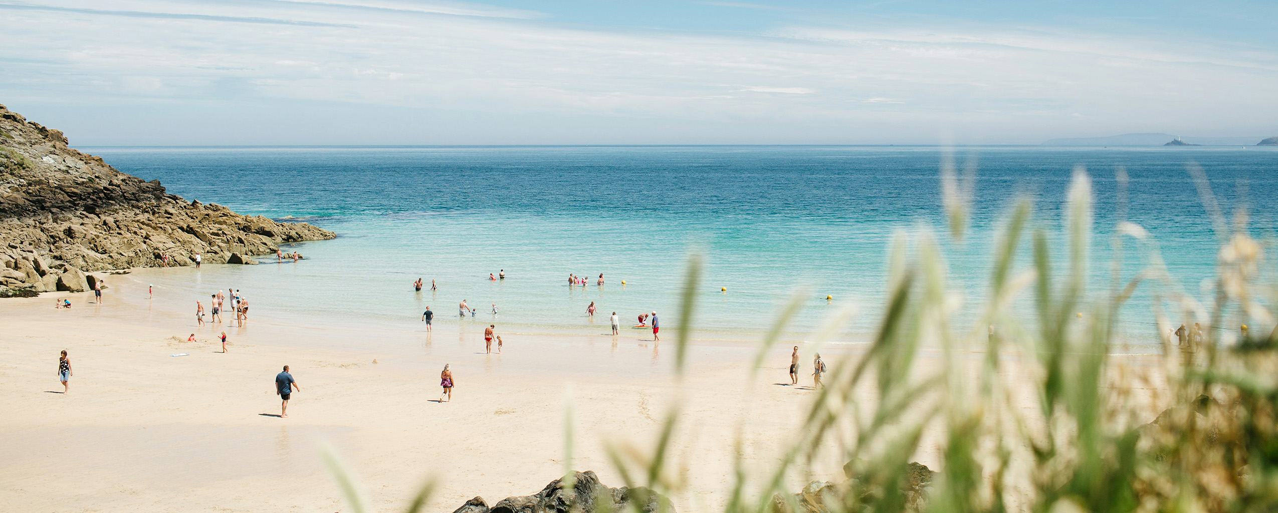 A lively group of people enjoying a sunny day at Porthgwidden Beach, with the sparkling water in the background, discover this location after browsing your guest booking terms and conditions.
