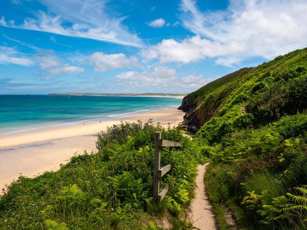 A scenic coastal path winding through greenery, leading to the sparkling ocean at Carbis Bay, a storied part of Carbis Bay's arts and heritage.