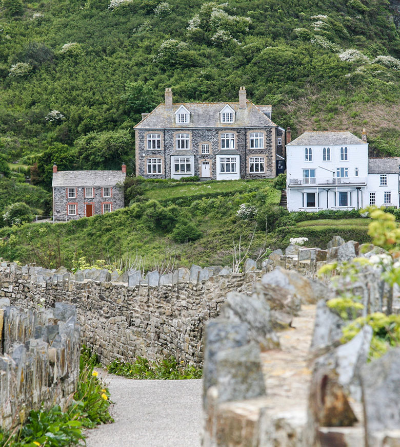 A charming stone wall with a path leading to the cottages used when filming 'Doc Martin' in Port Isaac, surrounded by lush greenery.