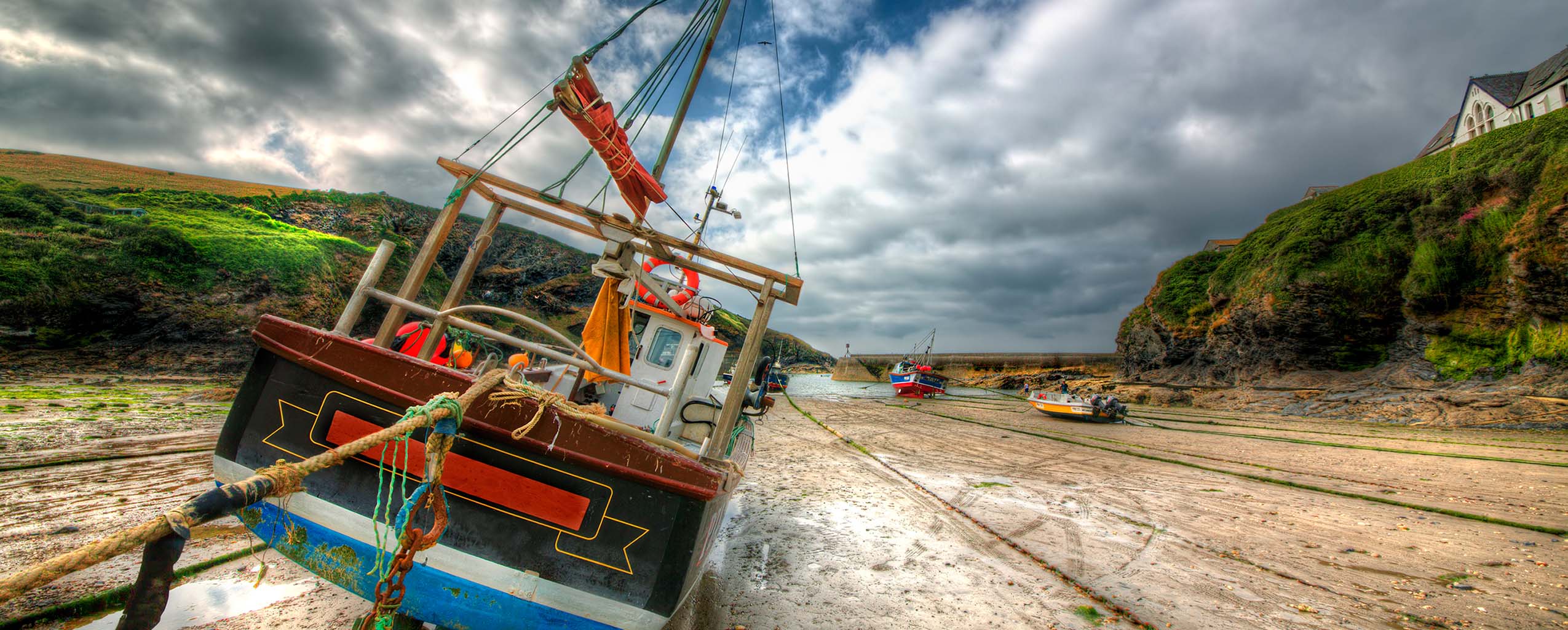 A fishing boat rests on the rocky shore of Port Isaac Harbour, surrounded by gentle waves and scenic coastal views, a part of Port Isaac's arts and heritage.