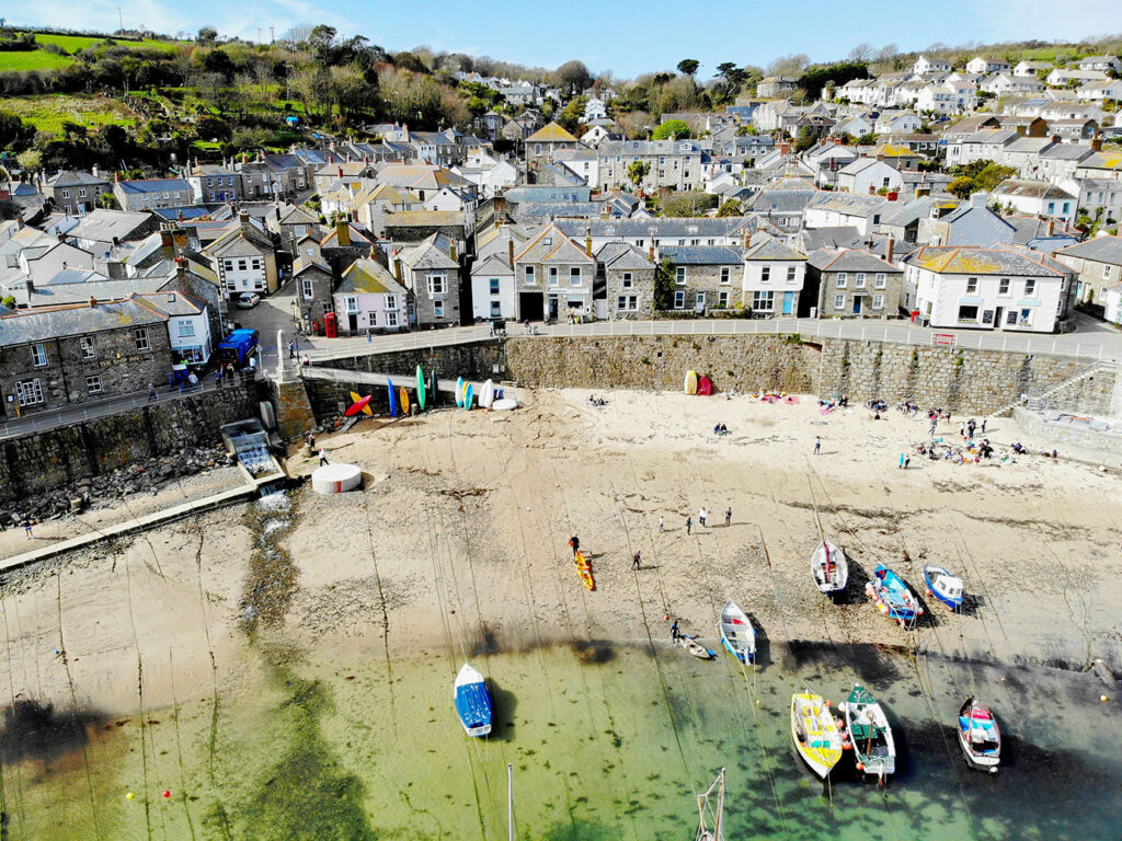 Scenic view of Mousehole Harbour, featuring a sandy beach and colorful boats bobbing in the calm waters, a key part of the heritage in Mount's Bay.