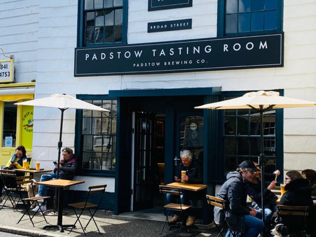 Diners enjoy meals outside the Padstow Brewing Co in Padstow, shaded by colourful umbrellas on a sunny day, a great food and drink option in Padstow.
