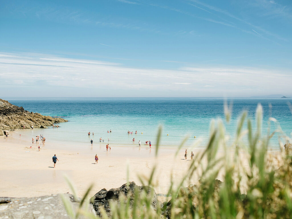 People relax and enjoy the sunny day at Porthgwidden Beach in St Ives, surrounded by golden sand and clear blue water, it also has many great food and drink options.