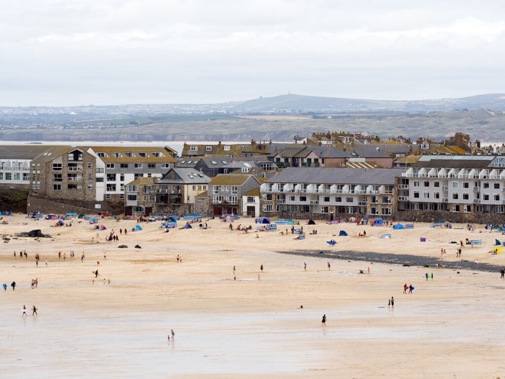 A sunny Porthmeor Beach in St Ives, featuring golden sand and gentle waves, perfect for relaxation and seaside fun, it also has many great food and drink options.