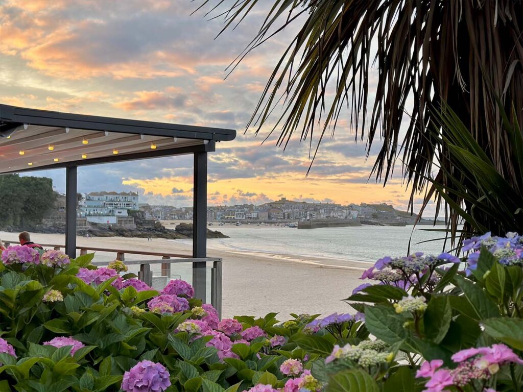 A beach gazebo adorned with flowers, set against a stunning sunset at Porthminster Café in St Ives, a great place for food and drink in St Ives.
