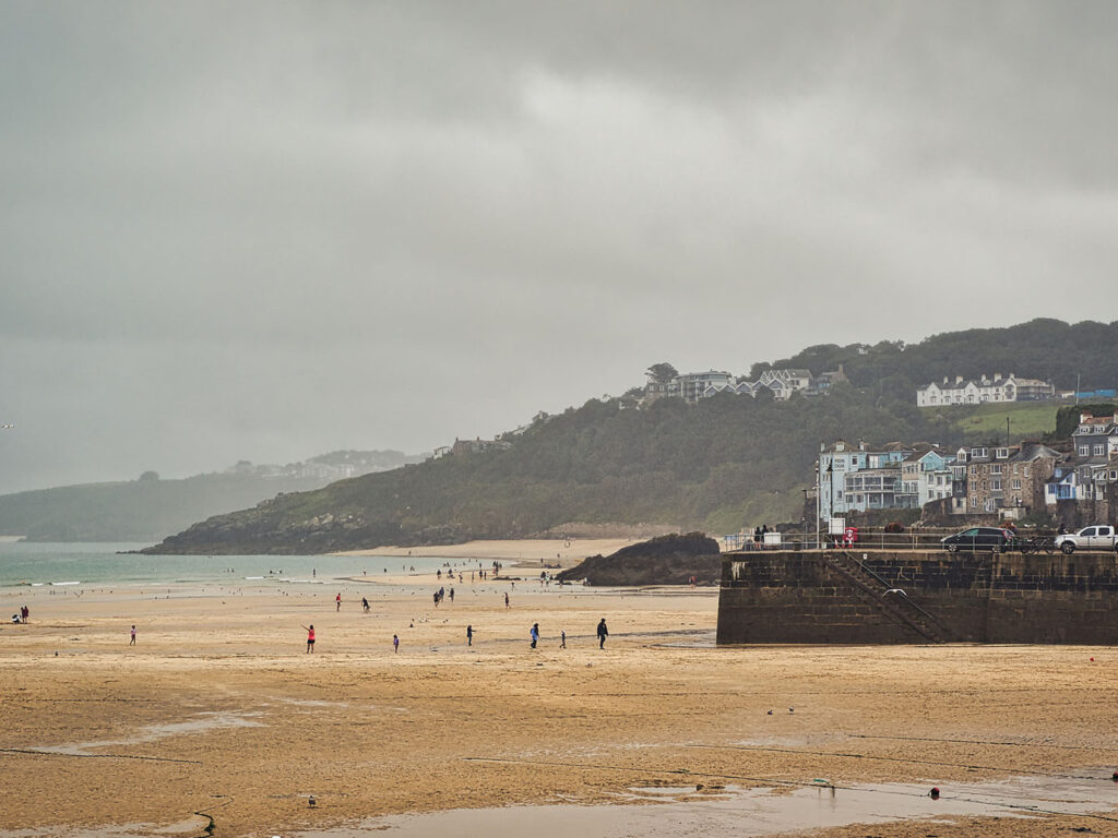 St Ives Harbour on a cloudy day, featuring people strolling along the beach with buildings in the background, St Ives has lots of arts and heritage.