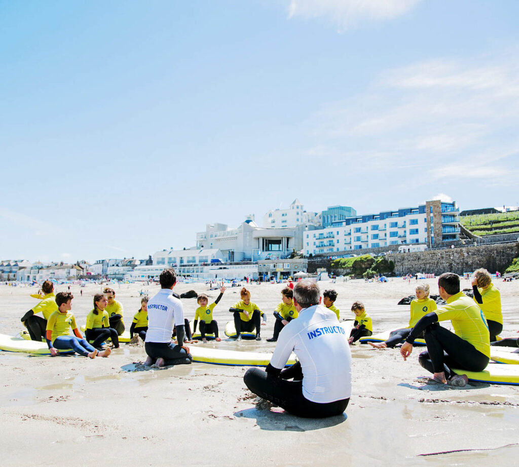 A group of people relaxing on the beach with surfboards, enjoying a sunny day at St Ives Surf School, a great thing to do in Cornwall with the kids this Summer.