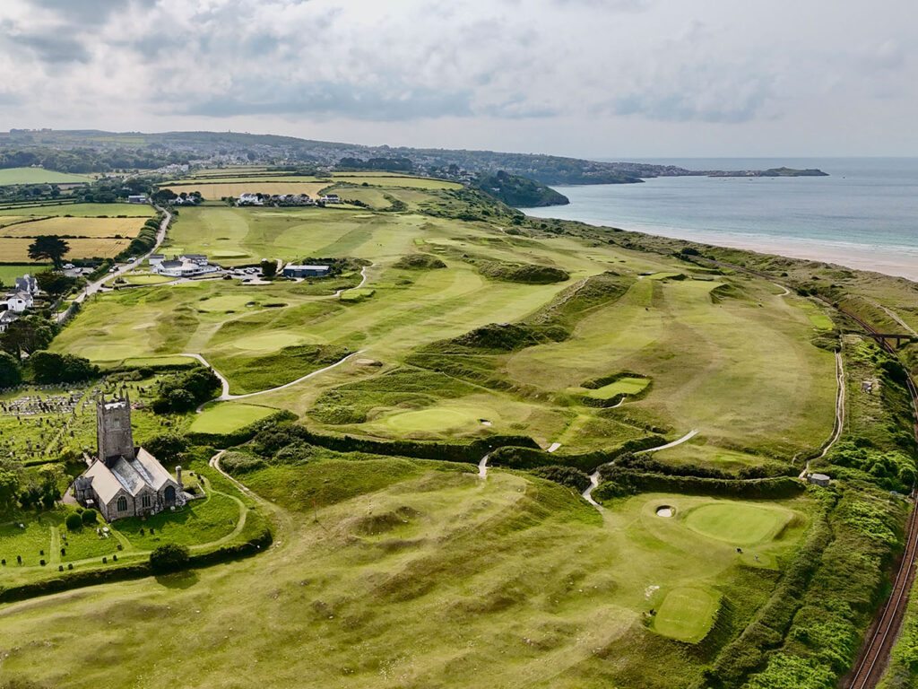 Aerial view of St Uny Church and the beach in Lelant, showcasing the scenic coastline and the nearby West Cornwall Golf Club, close to many Lelant food and drink options.
