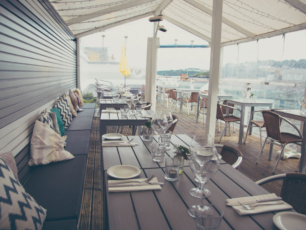 Outdoor dining area at The Loft St Ives, featuring tables and chairs on a sunny deck overlooking the scenery, a great place for food and drink in St Ives.