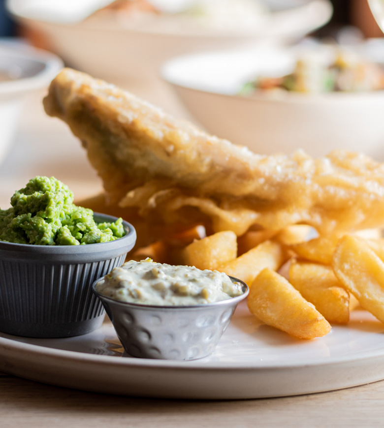 A tempting plate of fish and chips, featuring a bowl of dip and a side of golden fries, ideal for enjoying in St Ives.