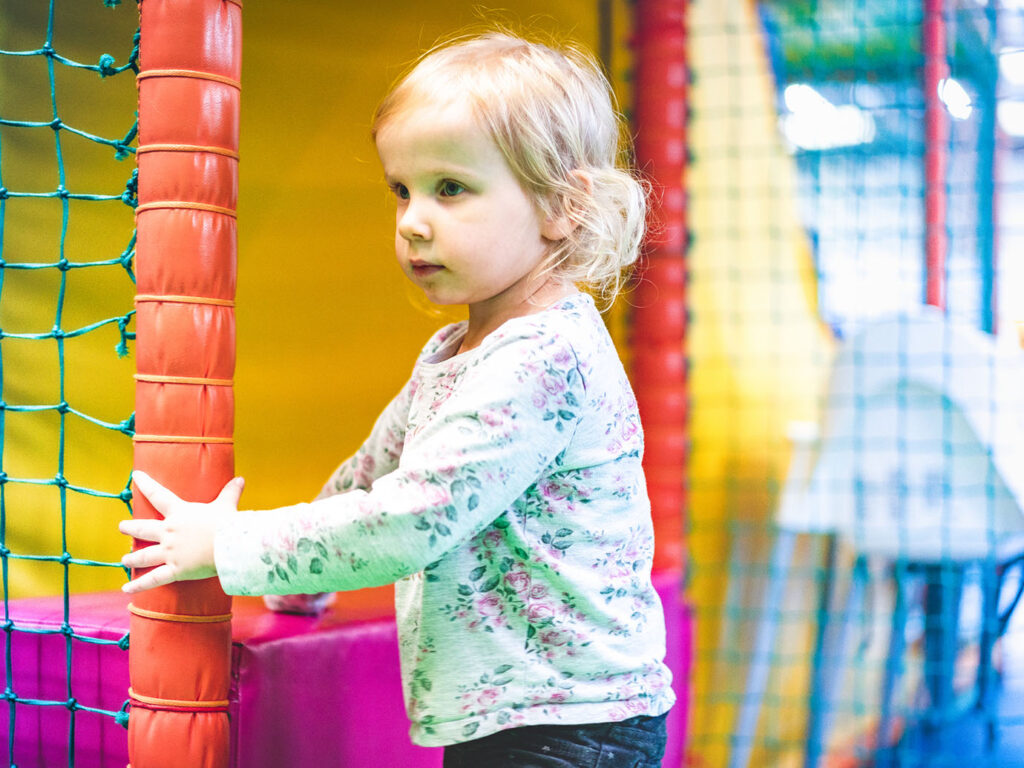 A young girl joyfully stands in a colourful soft play centre, surrounded by climbing structures and soft toys, a great Cornish Day Out.