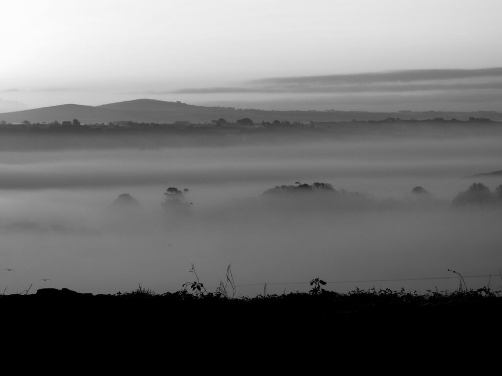 Black and white photo of misty hills overlooking Lelant, Cornwall, shrouded in fog, creating a serene landscape, there are many places for food and drink in Lelant.