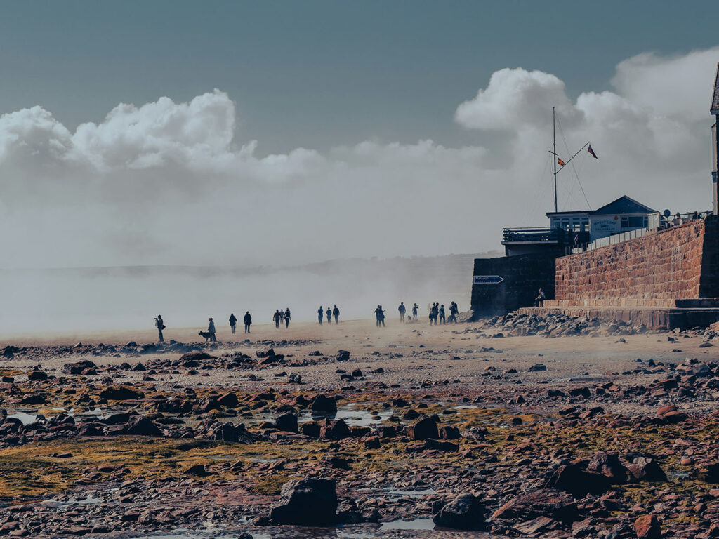 A cloudy sky looms over Marazion Beach, where people enjoy the seaside atmosphere and activities, adjacent to some great food and drink locations in Marazion.