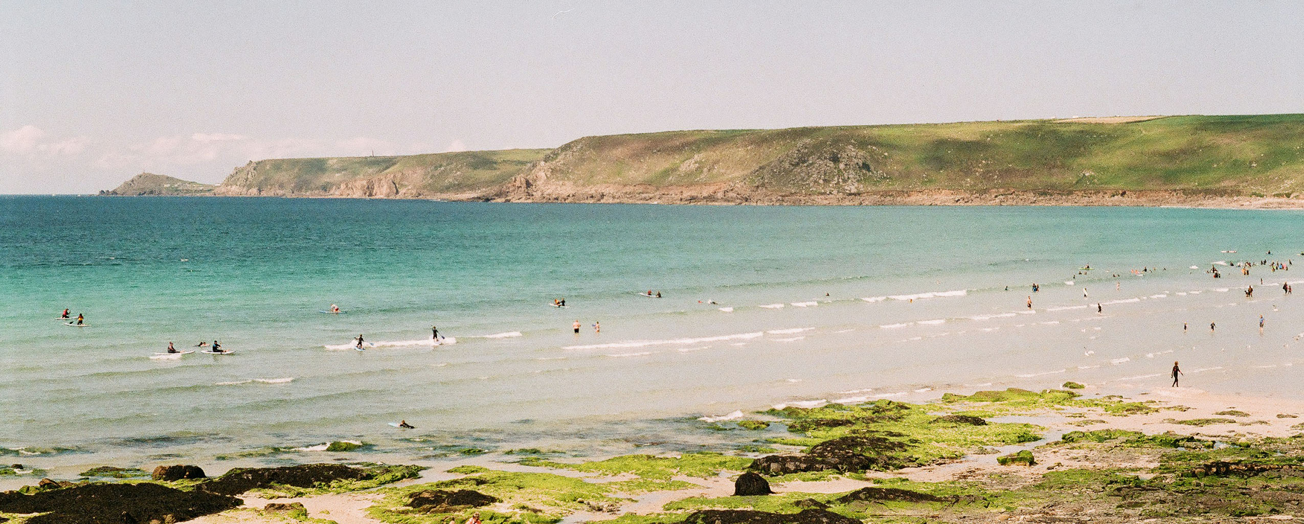 Sennen Cove Beach in Cornwall, featuring people swimming in the water and others relaxing on the sandy shore, a great place to vbisit from a Cornwall Holiday Cottage.