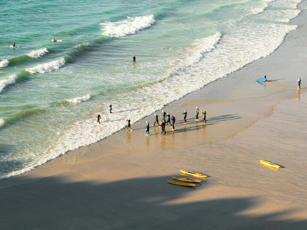 A lively beach scene at St Agnes with surfers and swimmers enjoying the sun and surf, surrounded by colourful surfboards, grab some food and drink in St Agnes after this tiring activity.