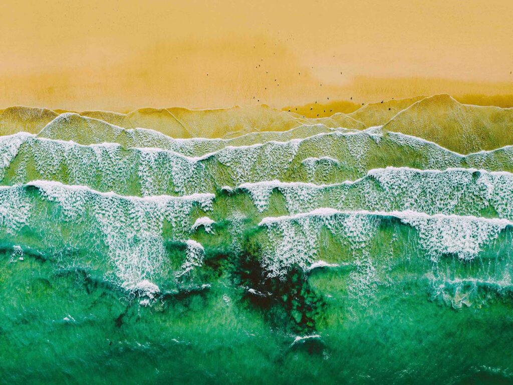 Aerial view of Carbis Bay Beach, showcasing vibrant blue ocean waves gently crashing on the sandy shore, a key part of the arts and heritage in Carbis Bay.