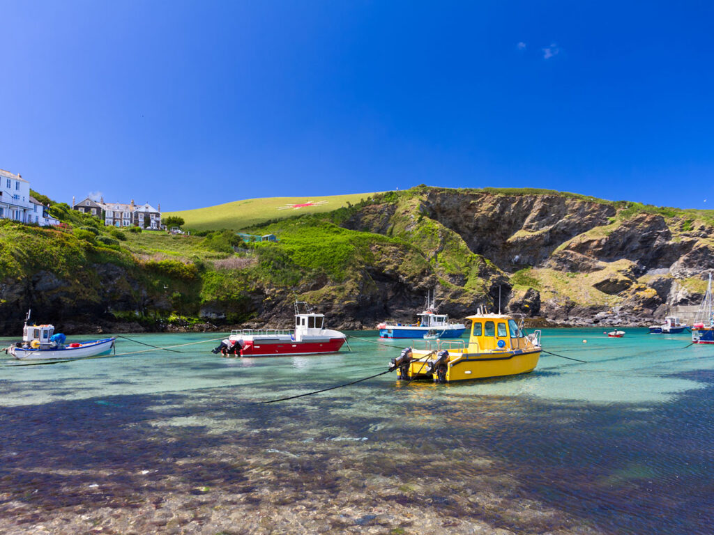 Boats gently bob in Port Isaac harbour under a bright blue sky with fluffy white clouds, these boats are integral to the food and drink in Port Isaac.