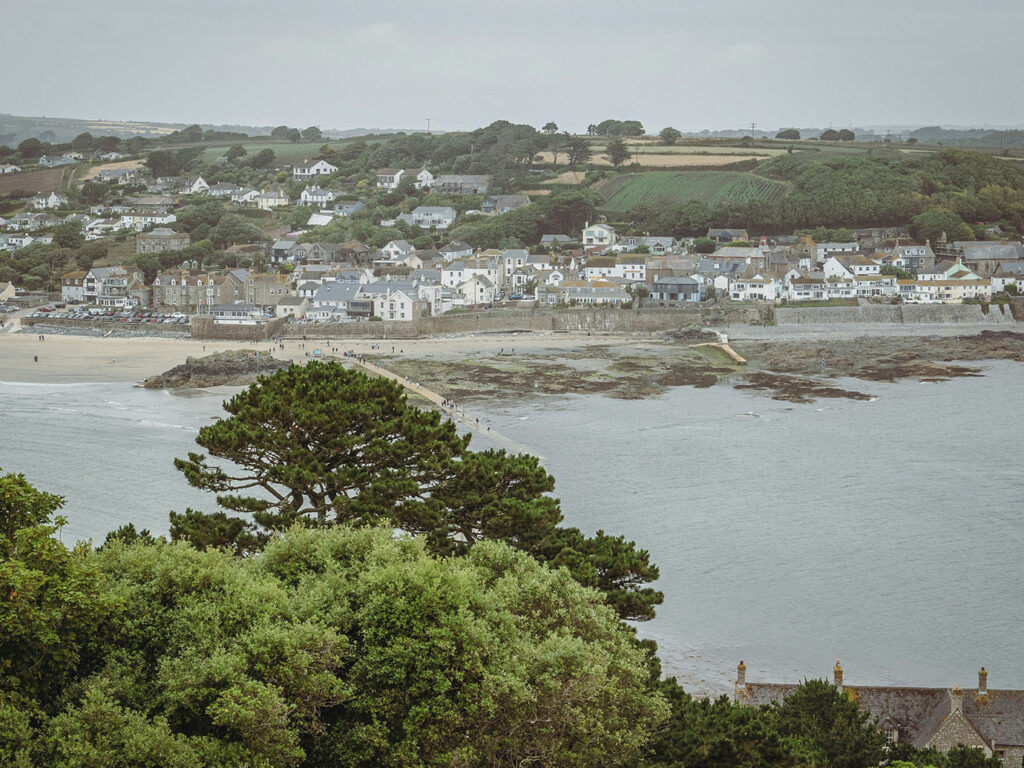 A scenic view of Marazion town and beach from a hill, showcasing the marshes and coastal landscape, and lots of food and drink options in Marazion.