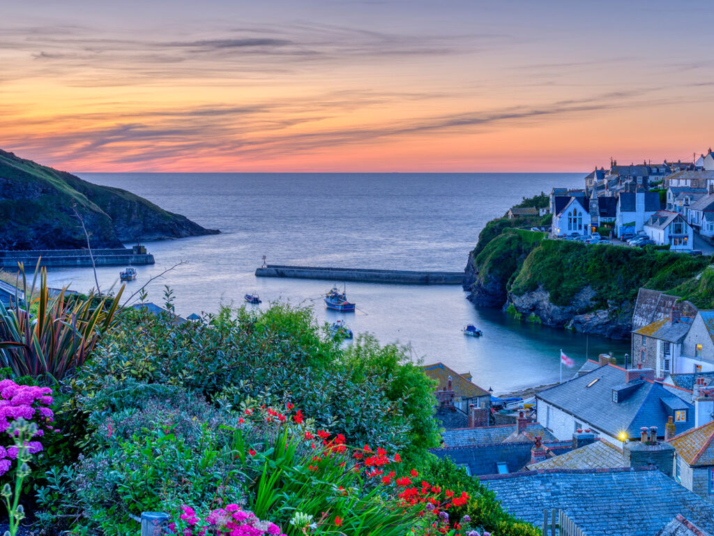 Sunset over Port Isaac, showcasing vibrant flowers in the foreground and the town's charming rooftops in the background, Port Isaac is a great place for food and drink.